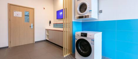 A laundry area with a washing machine, a dryer, a wooden door, and a blue-tiled wall.