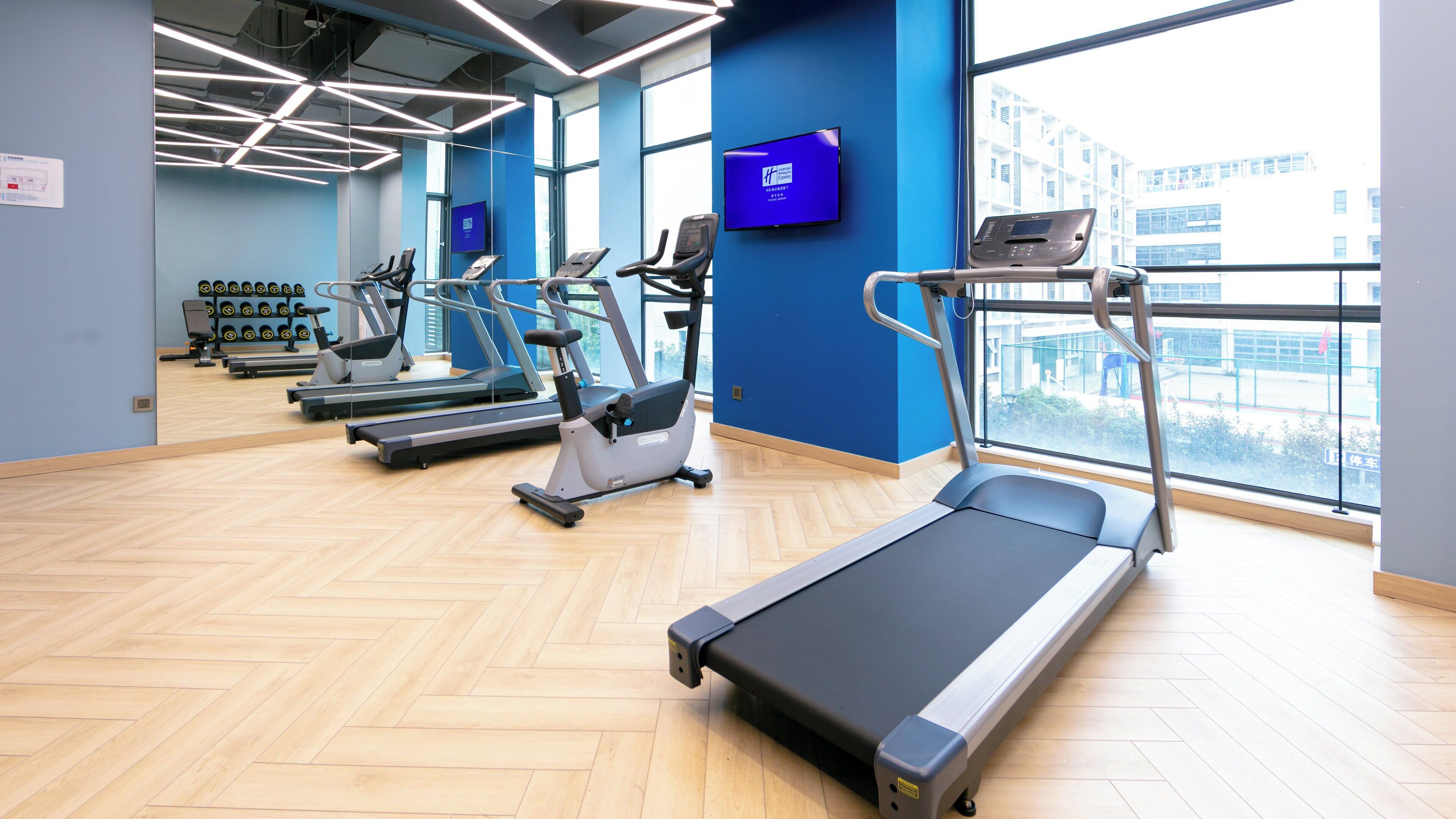 Un gimnasio con cintas de correr, bicicletas estáticas y un espejo grande.
