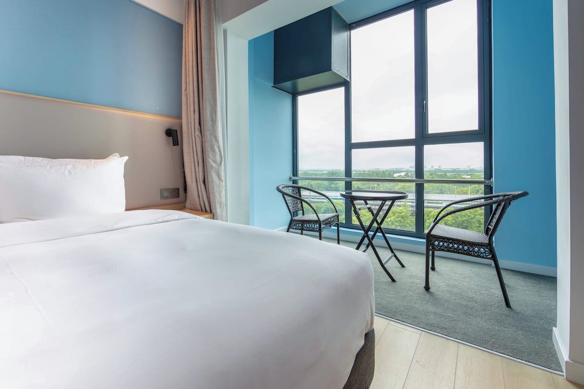 Une chambre d’hôtel avec un grand lit, un balcon avec deux chaises et une vue sur le paysage urbain.