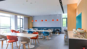 A modern dining area with multiple tables and chairs, a blue accent wall, and pendant lighting.