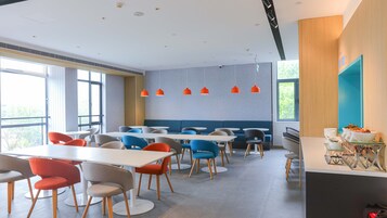 A modern dining area with multiple tables and chairs, a blue accent wall, and pendant lighting.