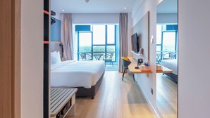 A modern hotel room with a large bed, a desk with a chair, a TV, and a balcony with a view. - Holiday Inn Express Shanghai Pudong Airport by IHG (Shanghai)