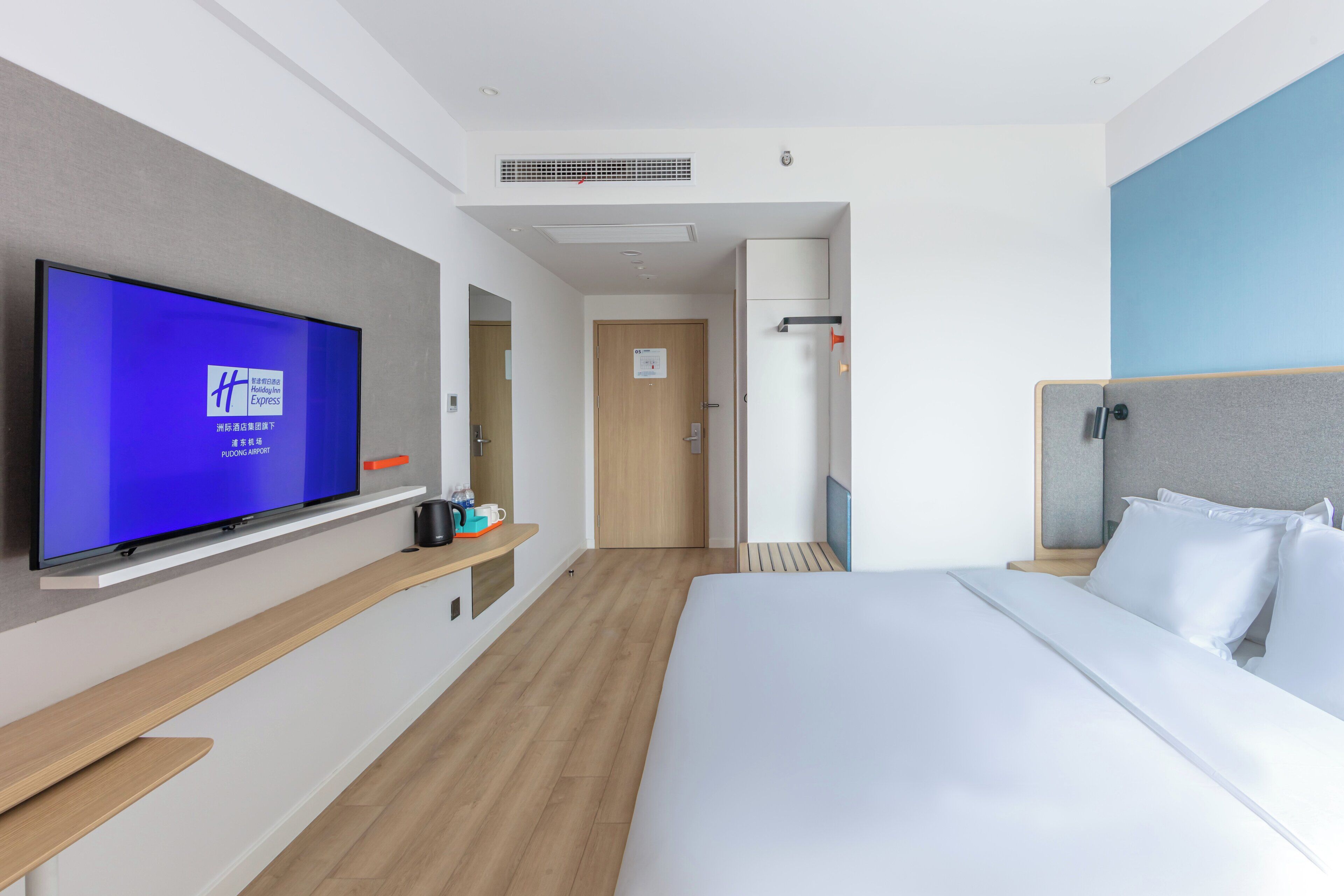 A modern hotel room with a large bed, a flat-screen TV on a wall, a wooden floor, and a small seating area.