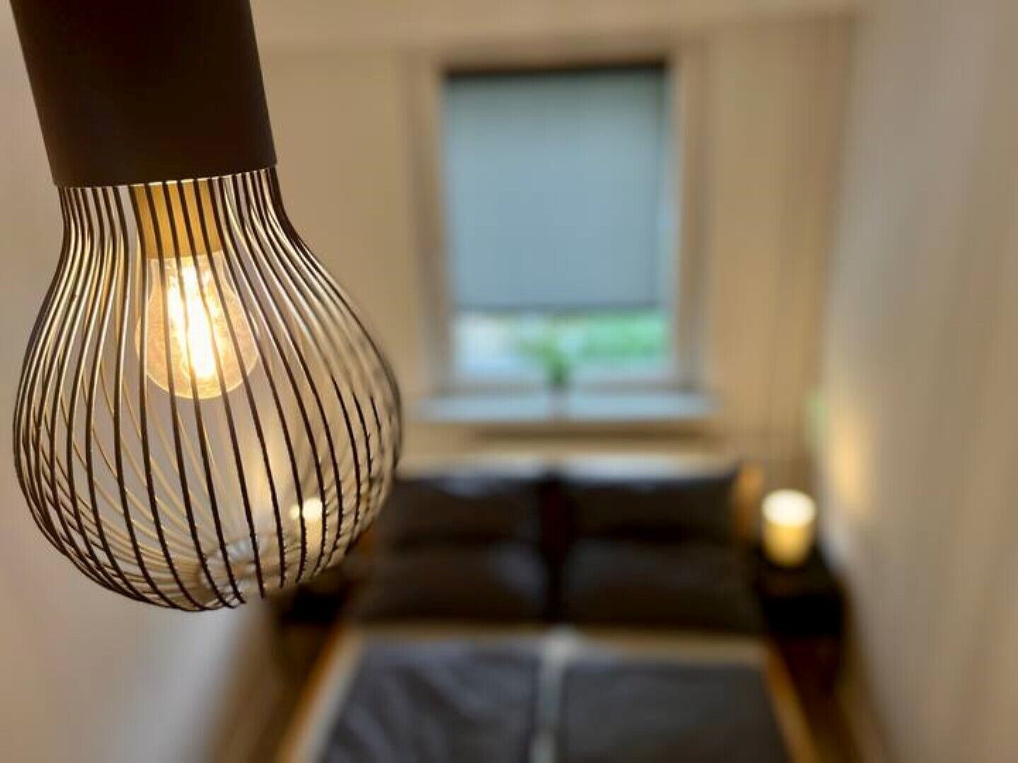 A modern room with a bed, a window with blinds, and a hanging light fixture.