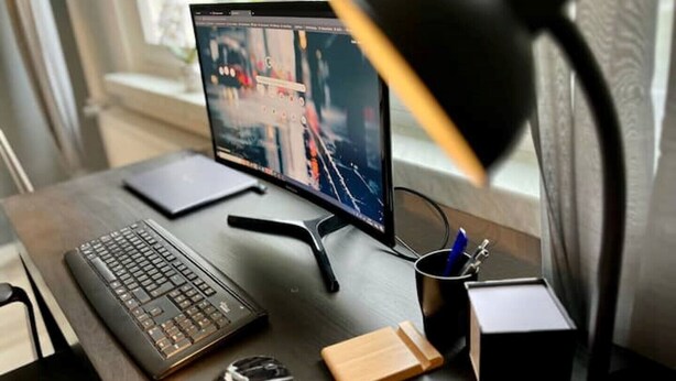 Un espacio de trabajo con una computadora portátil, teclado, ratón, lámpara de escritorio y una taza con un bolígrafo.