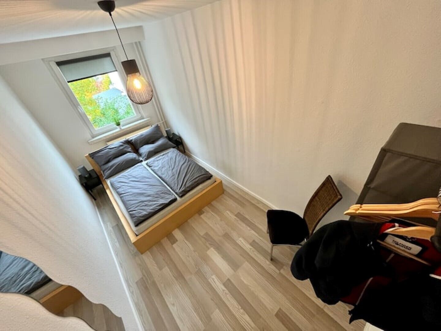 A bedroom with a bed, a window, a chair, and a wardrobe.