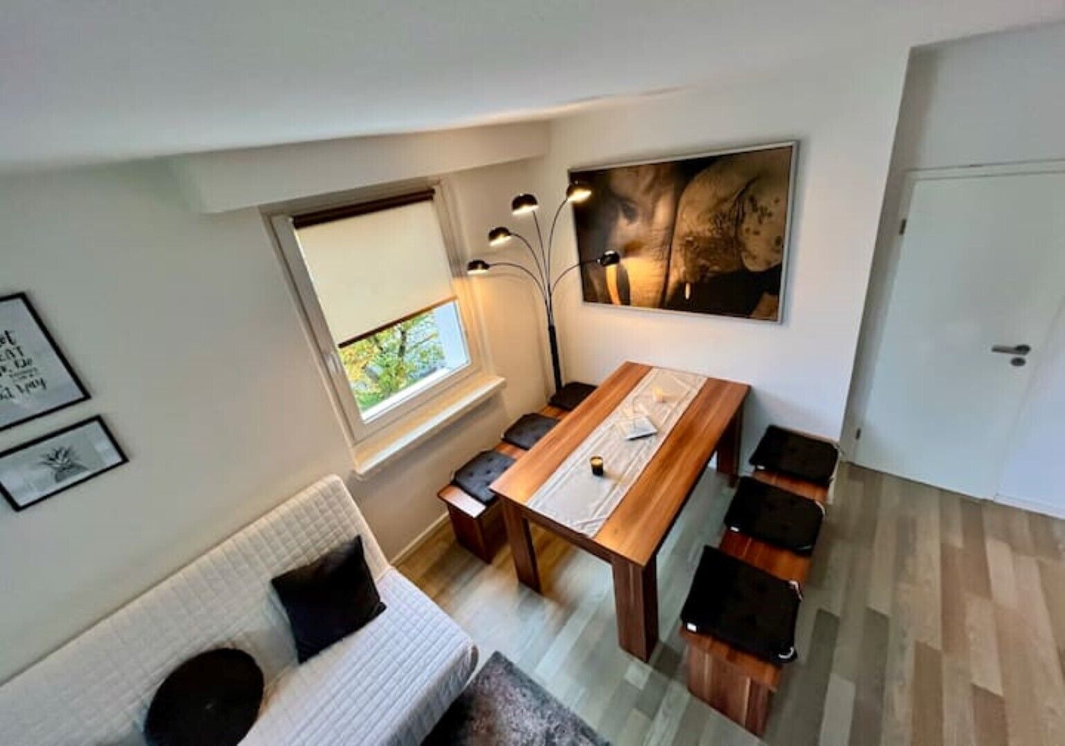A compact living space with a dining table, benches, a sofa, and a large window.