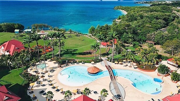 Un resort con una piscina grande, palmeras y vista al océano.