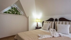 Habitación de hotel con cama, mesita de noche, lámpara y ventana con vista a palmeras.