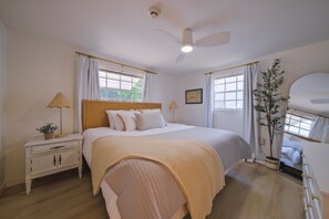 Relax in this serene bedroom with a large bed, ceiling fan, and natural light pouring in through the windows.