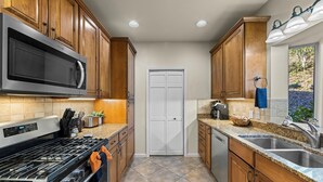A kitchen with wooden cabinets, a microwave, a stove, a sink, and a window with a view. - Condo w/ Creek, Golf & Mtn Views, Only 5 Steps to get in and Washer & Dryer! (Whittier)