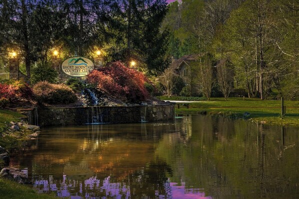 A serene landscape with a pond, a stone bridge, and a sign for Smoky Mountain Country Club.