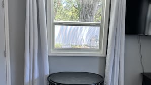 Una habitación con ventana, cortinas blancas, una mesa redonda con dos sillas y un televisor de pantalla plana en la pared.