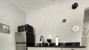 Una cocina moderna con un refrigerador de acero inoxidable, un microondas, una cafetera y armarios blancos.