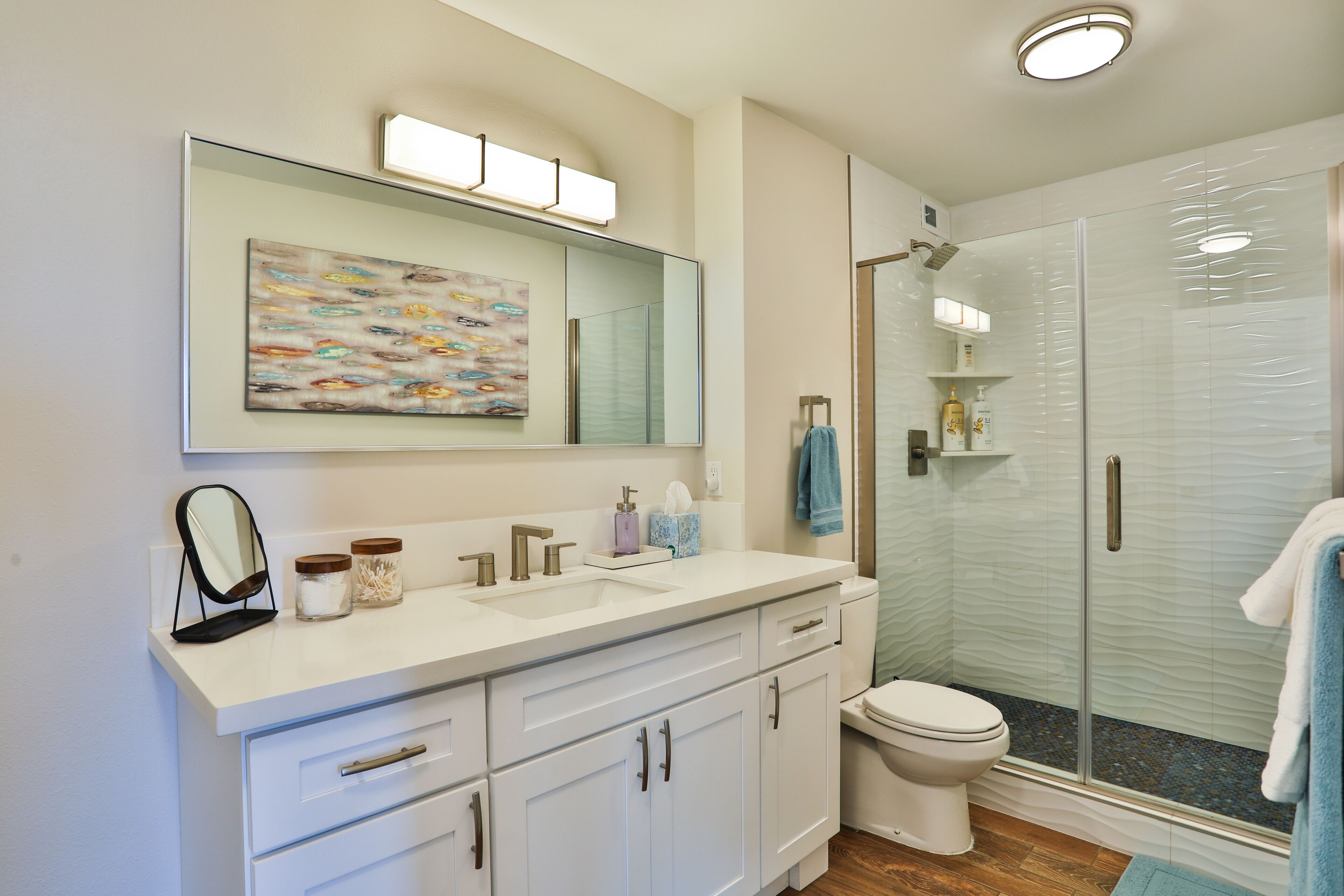 Une salle de bain moderne avec une douche à parois de verre, un grand miroir et un meuble-lavabo blanc doté d’un évier et d’armoires.