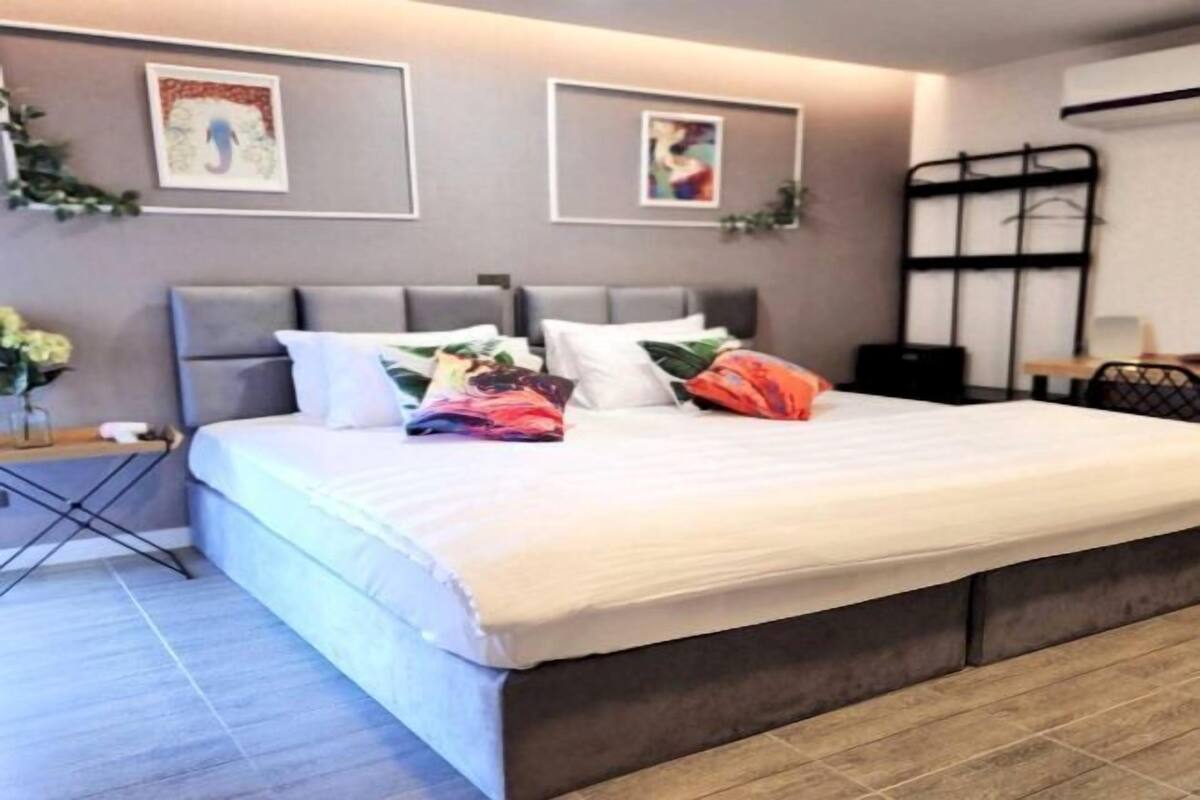 Een moderne slaapkamer met een groot bed, een grijs hoofdeinde en twee ingelijste foto’s aan de muur.