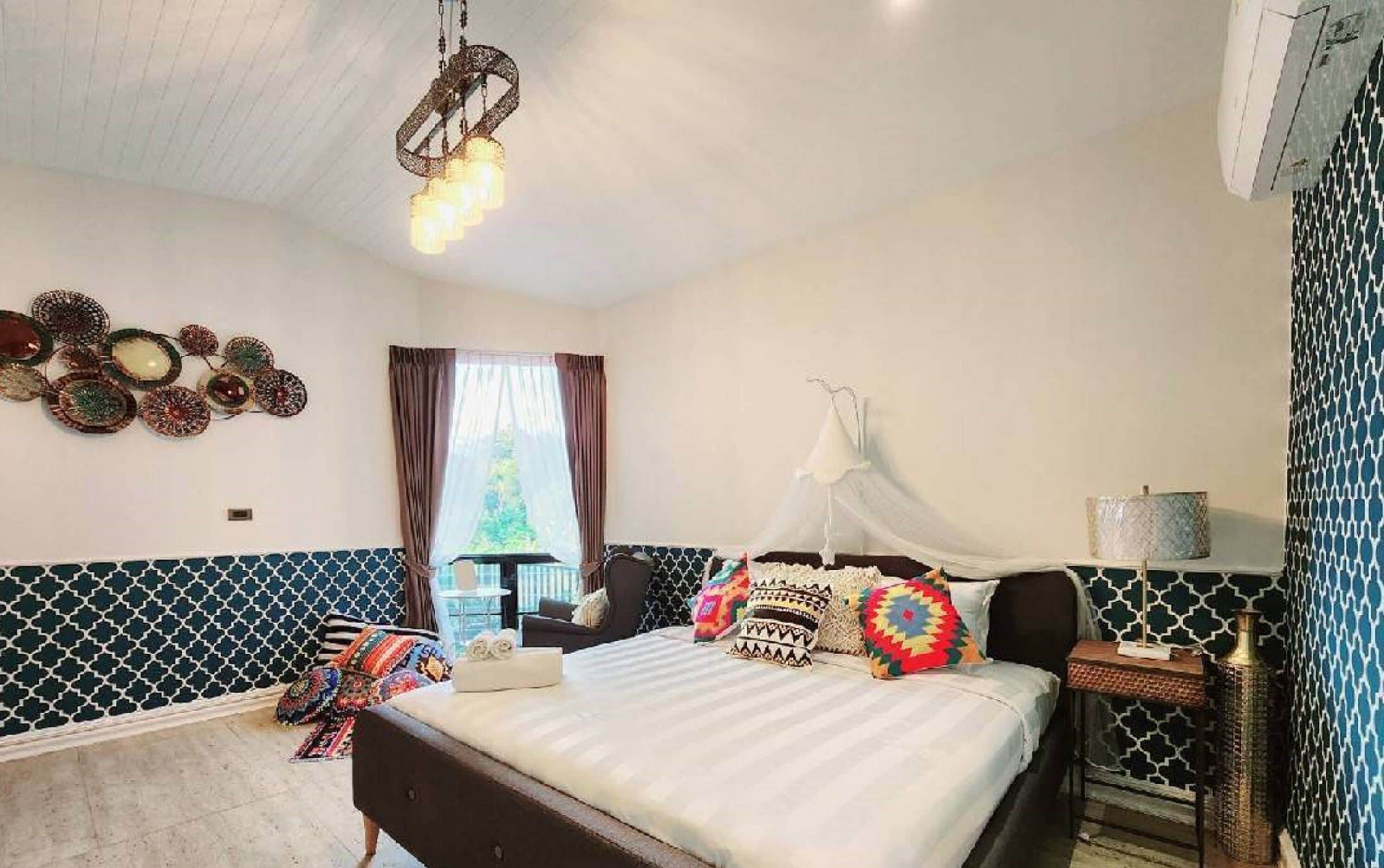 Une chambre à coucher avec un lit, une table de chevet, un luminaire suspendu et une fenêtre avec des rideaux.
