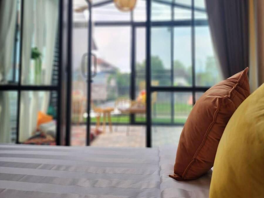 Una habitación con cama, almohadas y un ventanal con vistas al exterior.