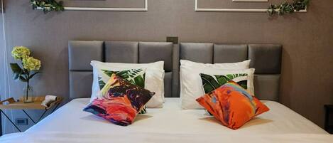 A hotel room with a bed, two framed artworks on the wall, and a bedside table with a vase of flowers.