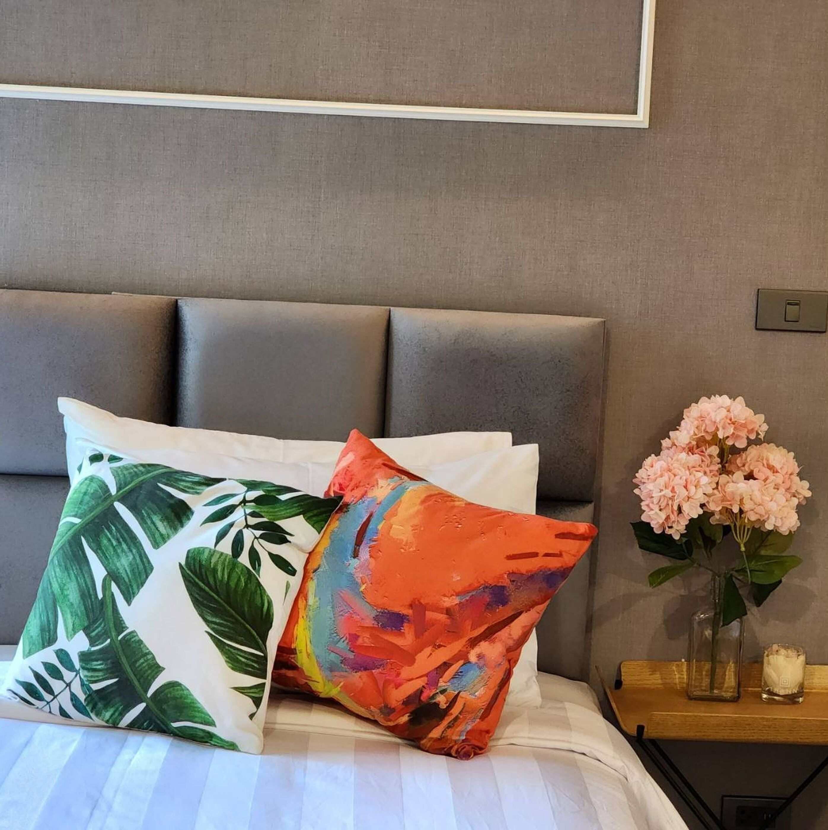 Una cama con varias almohadas, un jarrón con flores y una mesita de noche con una vela.
