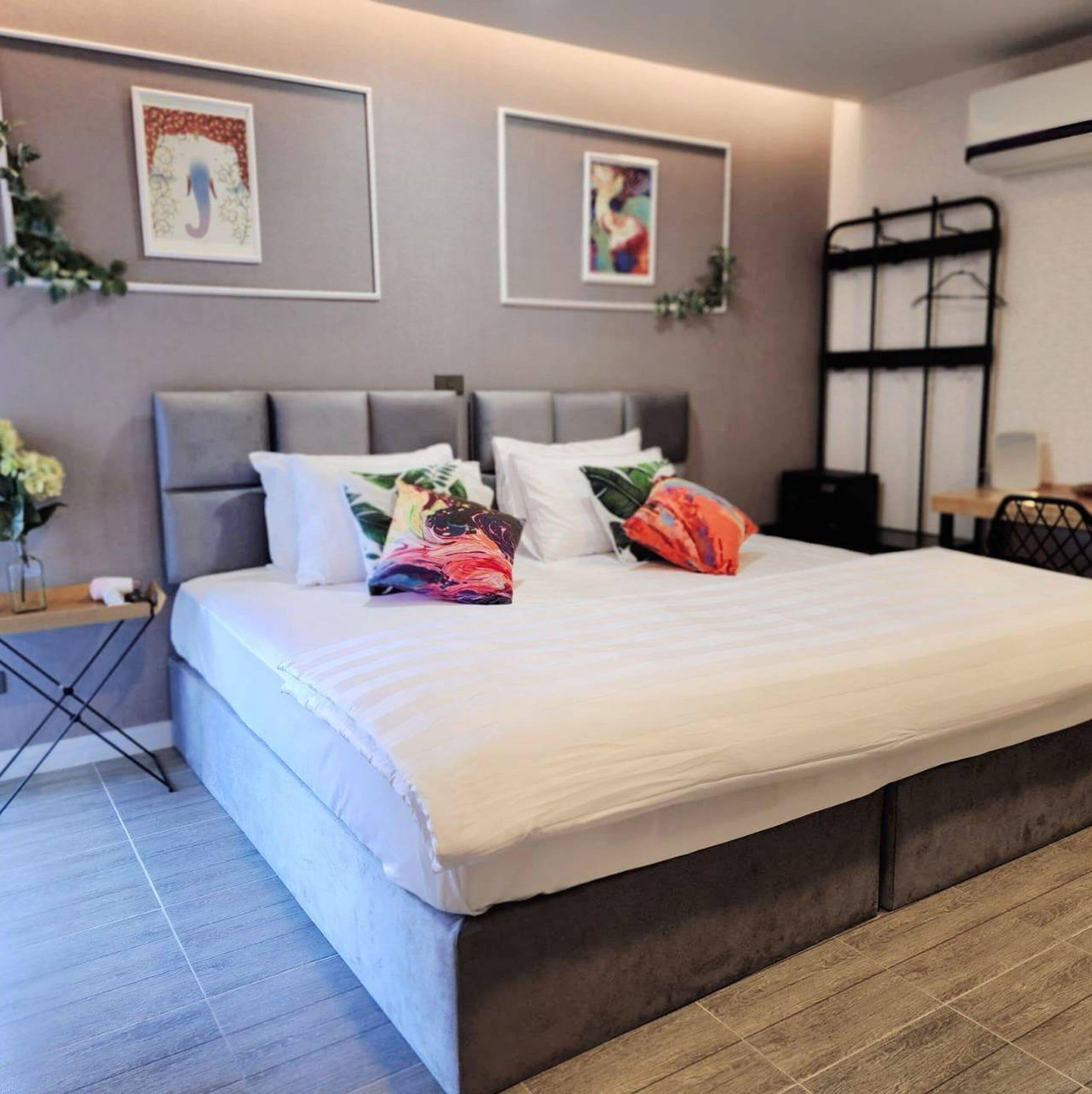 Une chambre à coucher moderne avec un grand lit, une tête de lit grise et deux œuvres d’art encadrées accrochées au mur.