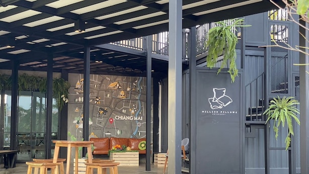 A modern outdoor seating area with wooden stools and a cushioned bench, a map mural on the wall, and a sign for 'Million Pillows Chiang Mai'. - Capital O 75422 Million Pillows  (Chiang Mai)