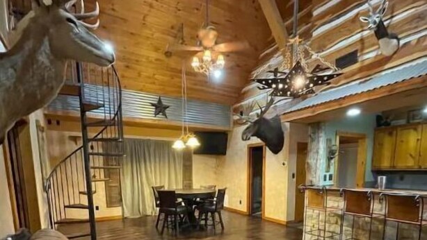 Amplia sala de estar con techo de madera, un sofá, comedor y cocina con barra.