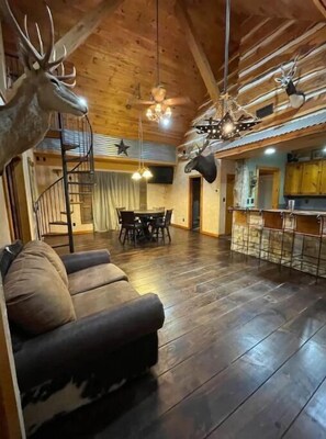 A spacious living room with a wooden ceiling, a sofa, a dining area, and a kitchen with a bar. - Trophy House (Aubrey)