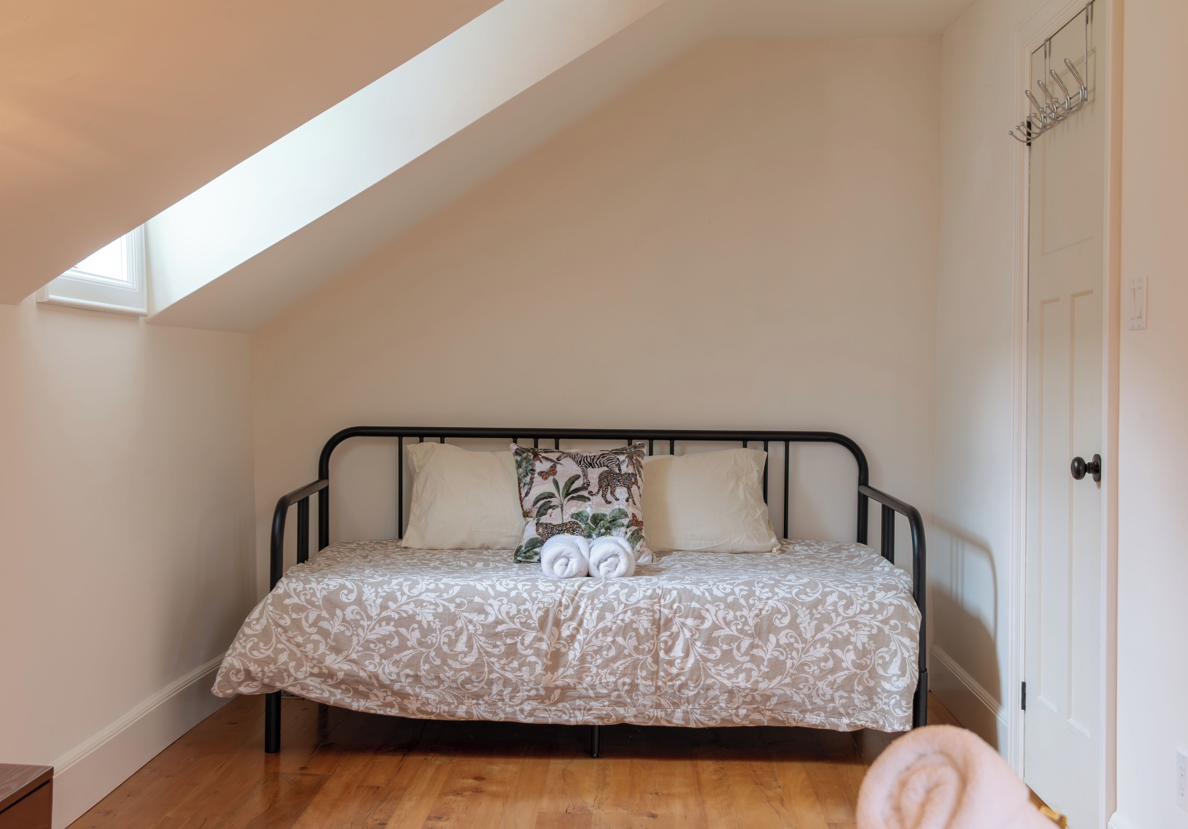 A bedroom with a sloped ceiling, a bed with a patterned bedspread, and a door with a coat rack.