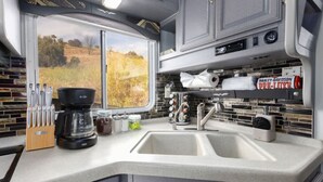 A compact kitchen with a window, a coffee maker, and a shelf with a Harley-Davidson can. - Harley Davidson Ranch Glampling & Kids Play Area (Ramona)