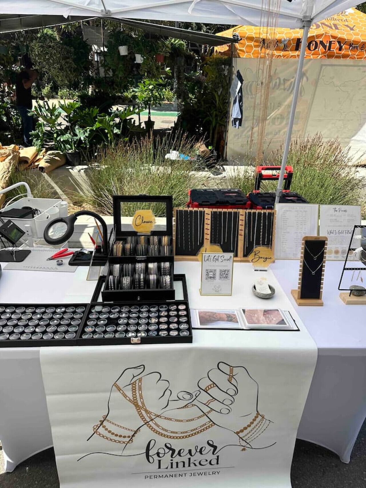 A jewelry display table with various items and a sign that reads "Forever Linked."