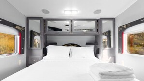 A modern train bedroom with a bed, bedside tables, and a window with a view. - Harley Davidson Ranch Glampling & Kids Play Area (Ramona)