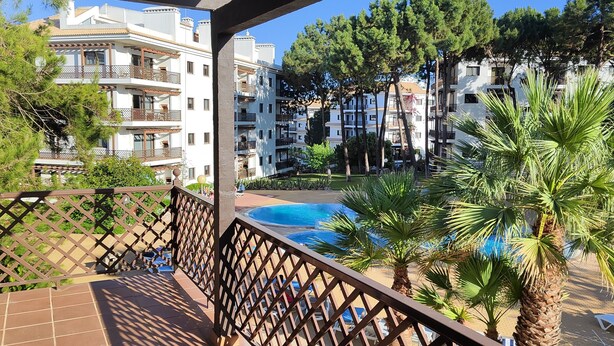 Un balcón con vista a una piscina, palmeras y edificios de varios pisos.
