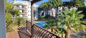 A balcony with a view of a swimming pool, palm trees, and multi-story buildings. - 2-Bedroom Apartment in Falésia, Algarve (Albufeira)