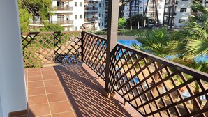 Un balcón con suelo de baldosas y barandilla de metal, con vistas a una piscina y un edificio con balcones.