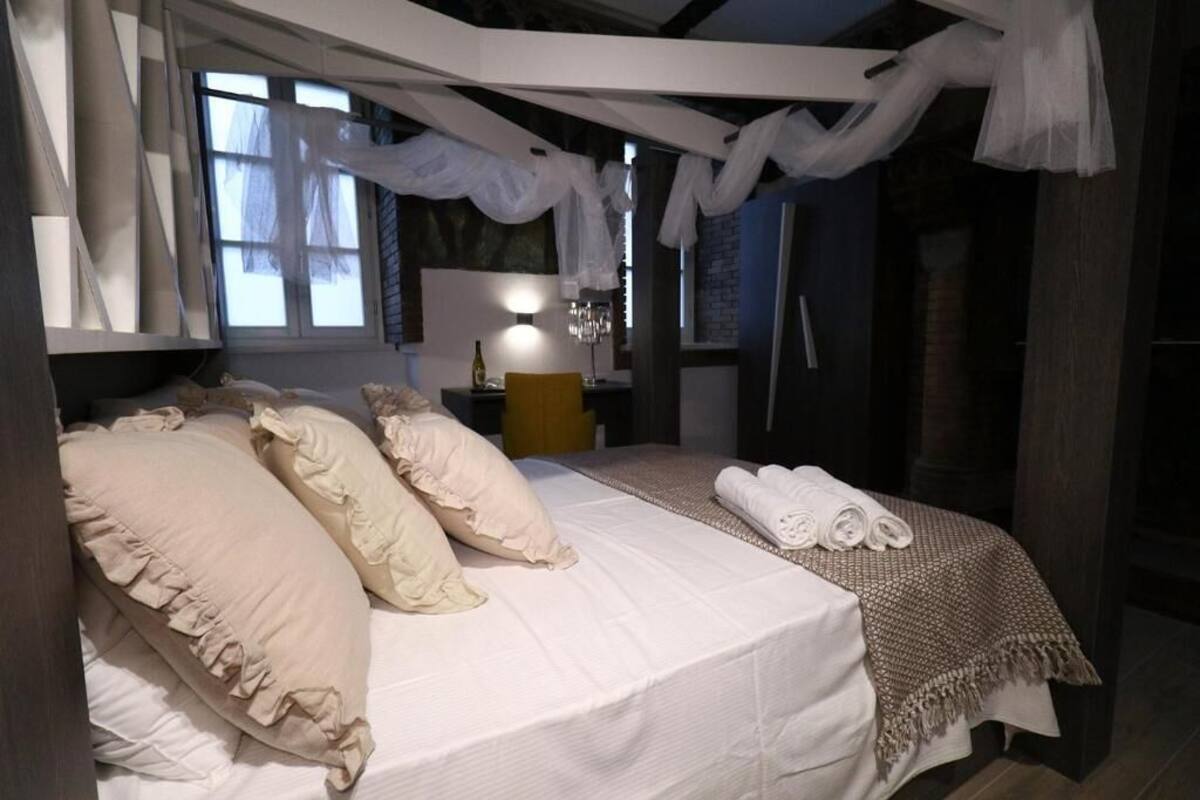 A bedroom with a bed, pillows, a bedside table with a lamp, and a window.