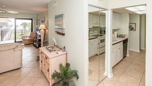 A living room with a sofa, a coffee table, and a dining area with a table and chairs. There is a kitchen with white cabinets and a stove. - Great Views Beach Vista at Ocean House 310 (St. Augustine)