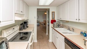 A compact kitchen with white cabinets, a stove, a sink, and a toaster. - Great Views Beach Vista at Ocean House 310 (St. Augustine)