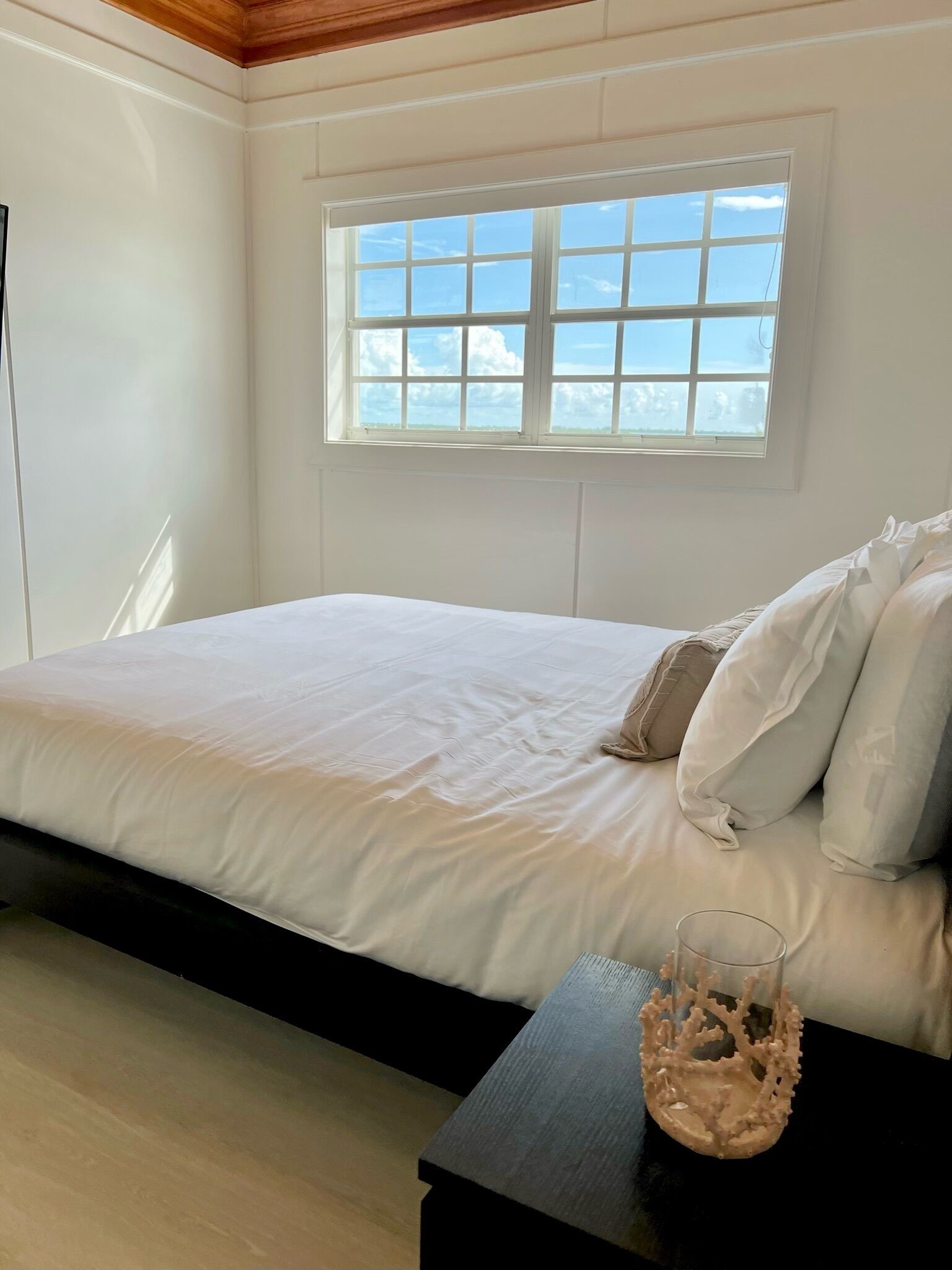 Ein Schlafzimmer mit einem Bett, einem Fenster und einem Nachttisch mit einer Glasvase.