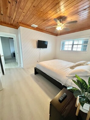 A bedroom with a bed, a ceiling fan, a TV mounted on the wall, and a window. - Your favorite getaway place (Bimini)