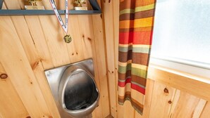 A wooden interior with a metal toilet, a window with a striped curtain, and a shelf with trophies. - Sugarloaf camp - ski/ outdoors rustic retreat (Carrabassett valley)