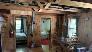 A wooden cabin interior with a dining area, a bed, and a bathroom. - Sugarloaf camp - ski/ outdoors rustic retreat (Carrabassett valley)