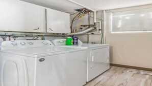 Un espace buanderie équipé d’un lave-linge et d’un sèche-linge à chargement frontal, d’un meuble de rangement au-dessus et de tuyauteries apparentes.