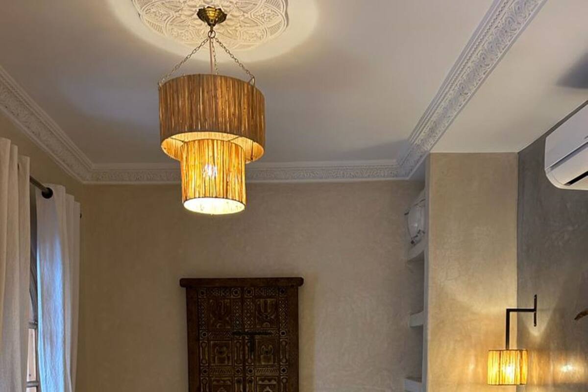 A hotel room with a large bed, a wooden headboard, a chandelier, a wall-mounted lamp, and a decorative wooden panel.