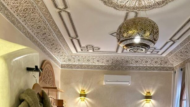 Une chambre à coucher avec un grand lit, deux lampes fixées au mur, un lustre et un banc en bois.