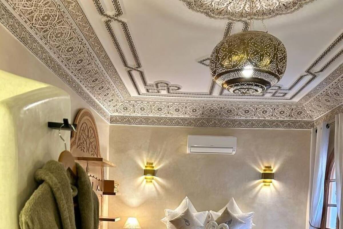 A bedroom with a large bed, two wall-mounted lights, a chandelier, and a wooden bench.
