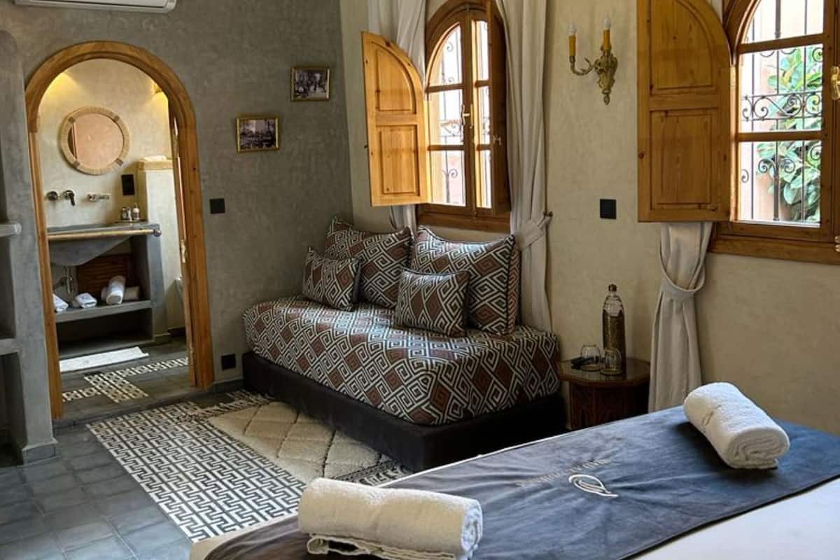 A bedroom with a large bed, a sofa, and a chandelier. There is a window with curtains and a door leading to a bathroom.