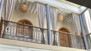 Un immeuble de deux étages doté d’un balcon, de balustrades en fer forgé décoratives et de tableaux encadrés accrochés au mur.