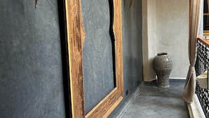Un couloir avec un mur de couleur gris foncé, un grand cadre en bois doté d’un motif en arc de cercle et un vase décoratif.