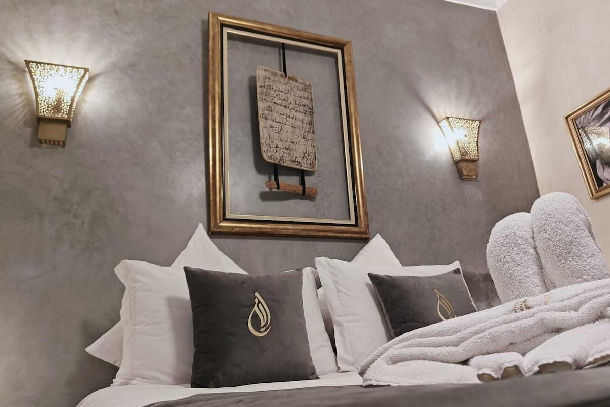 A modern bedroom with a grey wall, a framed piece of calligraphy, and two wall-mounted lamps.